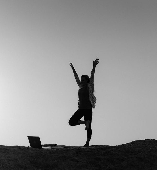 Silhouette of a person in a yoga warrior pose against a sunrise.